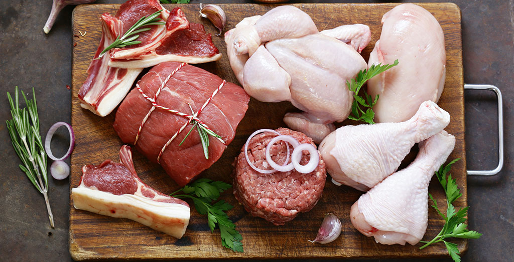 Various beautiful raw cuts of beef and chicken on cutting board with herbs and spices.